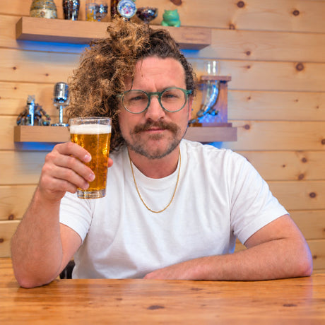 Aren Bane, Craft a Brew’s Senior Designer and Creative Director, raising a glass of beer in a wood-paneled room.