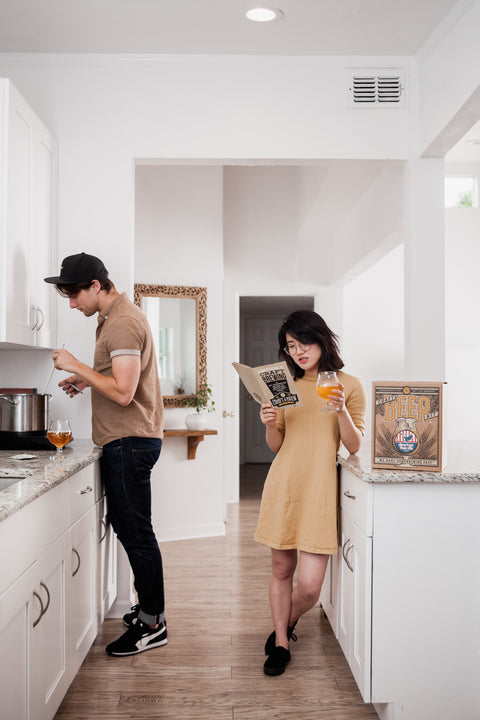 Two people brewing beer in a home kitchen with a Craft a Brew kit, one reading the brewing guide