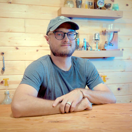 BC Phillips, Craft a Brew’s Head of Video, wearing a cap and glasses while seated at a wooden counter.