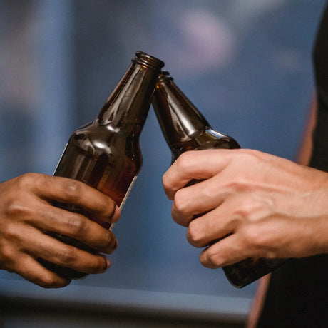 Two people clinking brown glass beer bottles.